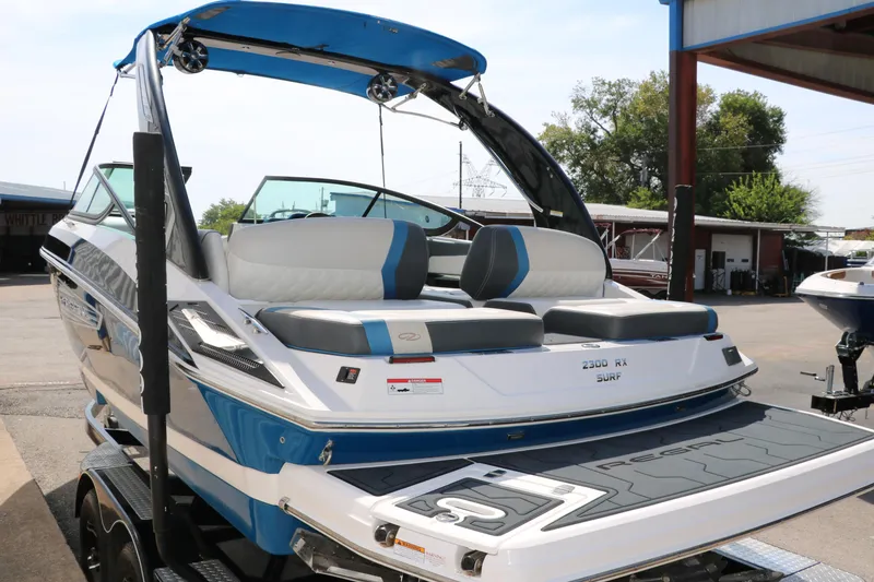 Slide: The Image of 2018 Regal 23 RX Surf boat with blue and white design, parked on a trailer. - 6