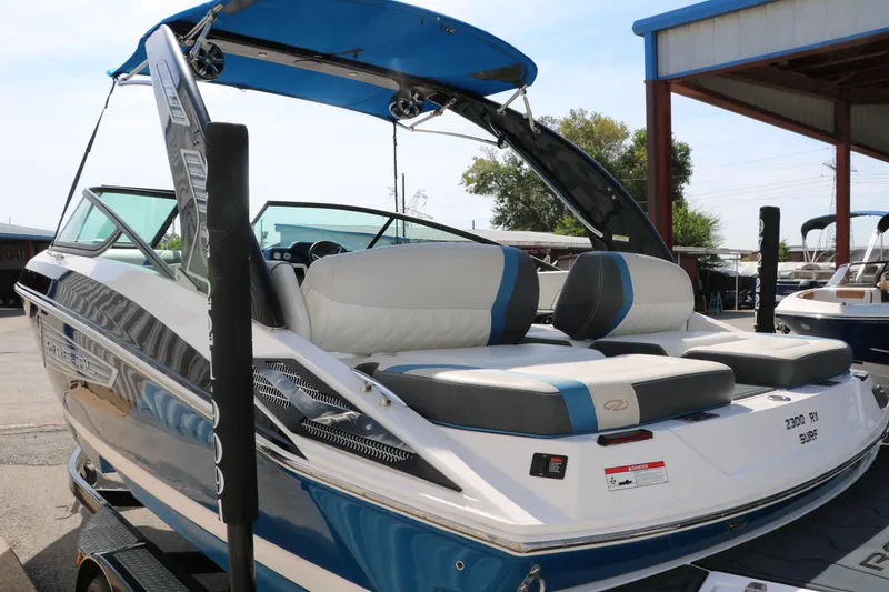 Slide: The Image of 2018 Regal 23 RX Surf boat with blue and white design, parked on a trailer. - 7