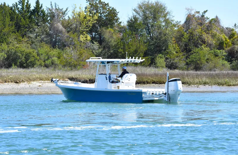 Slide: The Image of 2023 Pair Customs 24 Center Console MV boat on calm water near a wooded shoreline. - 5