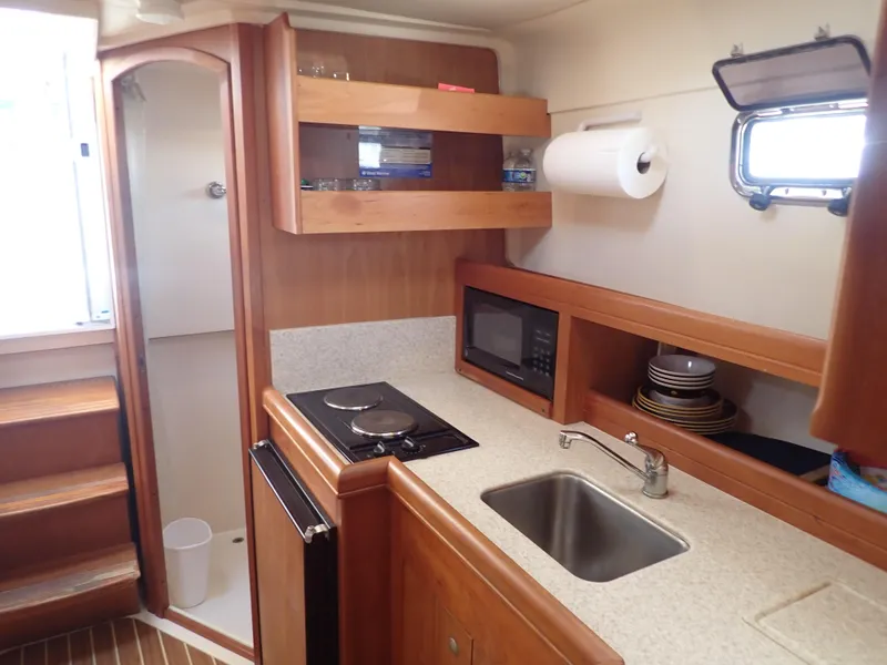 Slide: The Image of 2004 Mainship 34 Rum Runner II galley with stove, sink, microwave, and storage shelves. - 28