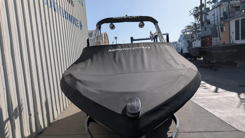 Slide: The Image of 2015 MasterCraft X10 boat with cover, docked near industrial buildings. - 34