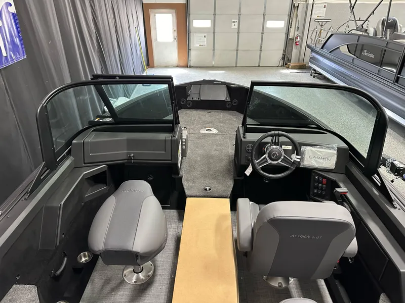 Slide: The Image of 2025 Alumacraft Competitor 185X Sport interior with dual seats and steering wheel in a showroom. - 12
