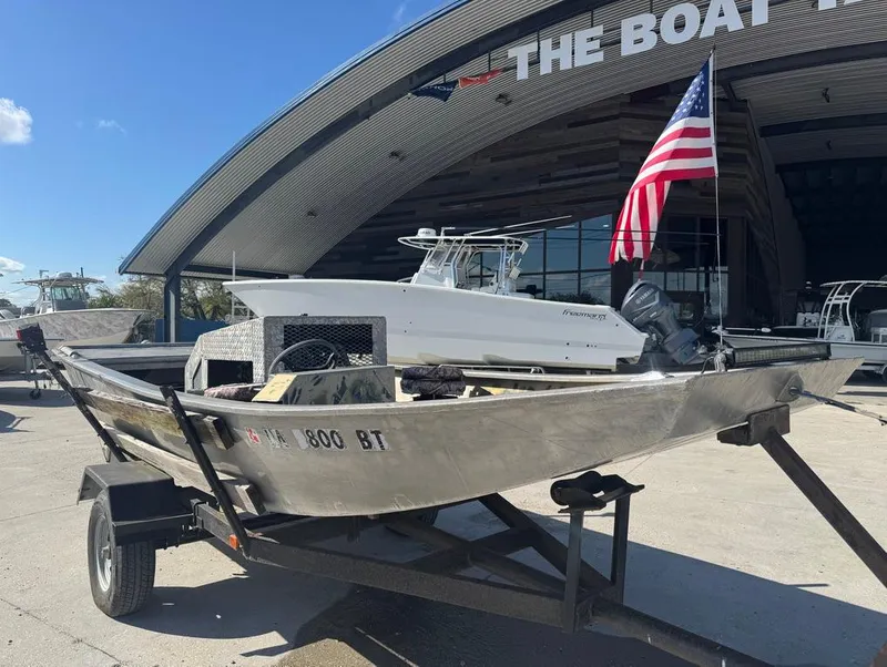 Slide: The Image of 1984 Custom Inboard Mud Boat on trailer, parked outside a boat dealership with American flag. - 2