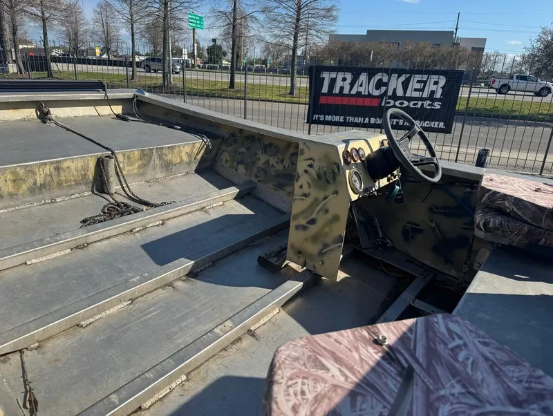 Slide: The Image of 1984 Custom Inboard Mud Boat with camo interior, parked near Tracker Boats sign. - 9