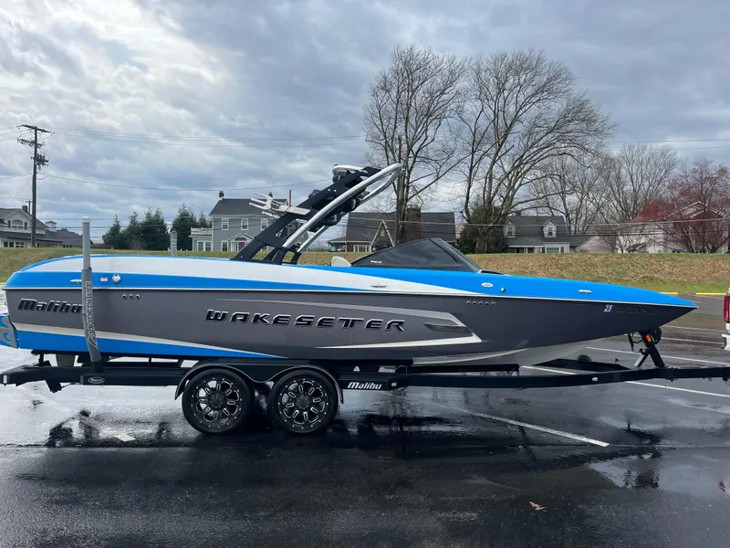 The Image of 2014 Malibu Wakesetter 24 MXZ boat on trailer, blue and gray design, parked outdoors. - 0