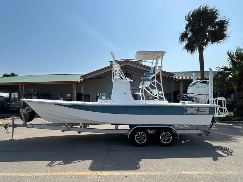 Slide: The Image of 2025 Shallow Sport 25 X3 boat on trailer, parked near a building with palm trees. - 0