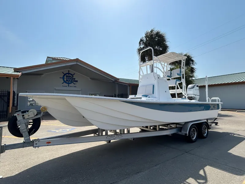 Slide: The Image of 2025 Shallow Sport 25 X3 boat on trailer, parked outside a building under clear sky. - 1