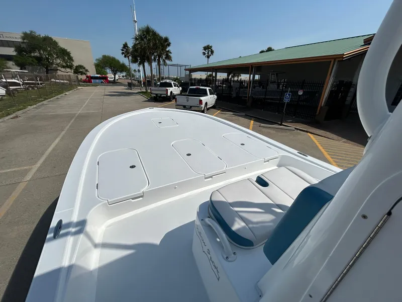 Slide: The Image of 2025 Shallow Sport 25 X3 boat with spacious deck, parked near palm trees and vehicles. - 20