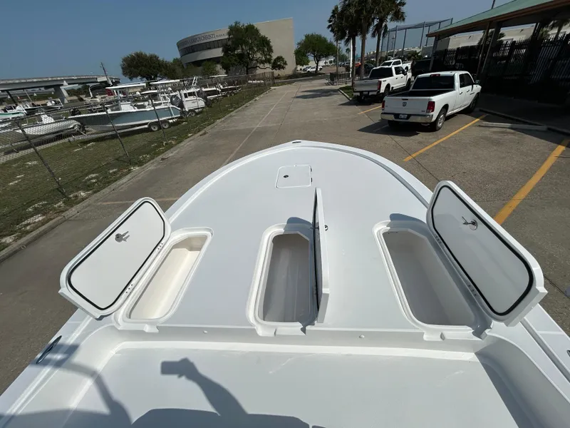 Slide: The Image of 2025 Shallow Sport 25 X3 boat deck with open storage compartments, parked outdoors. - 21