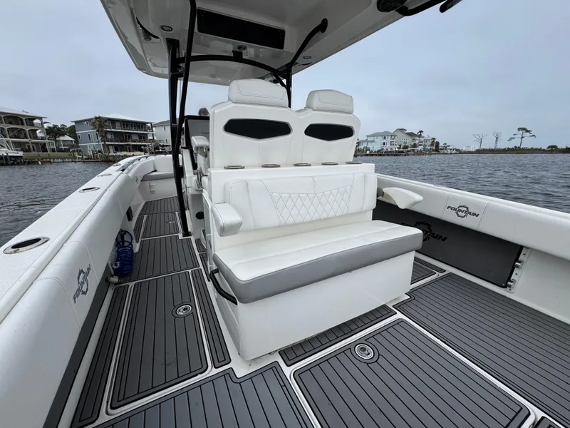 Slide: The Image of 2019 Fountain 34 CC boat interior with white seating and gray deck, docked by waterfront homes. - 32
