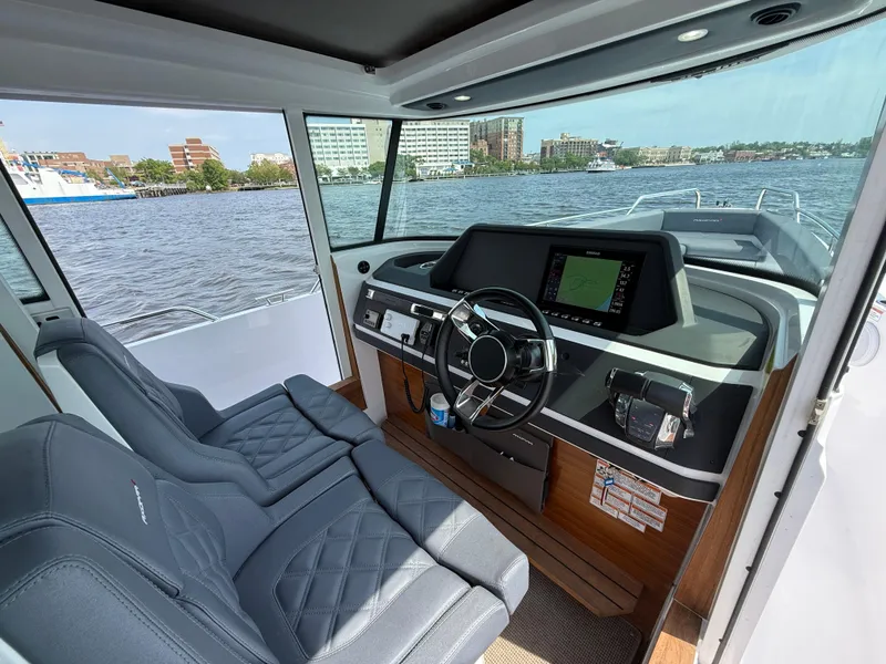 Slide: The Image of 2021 Axopar 28 CABIN interior with modern dashboard, steering wheel, and waterfront view. - 12