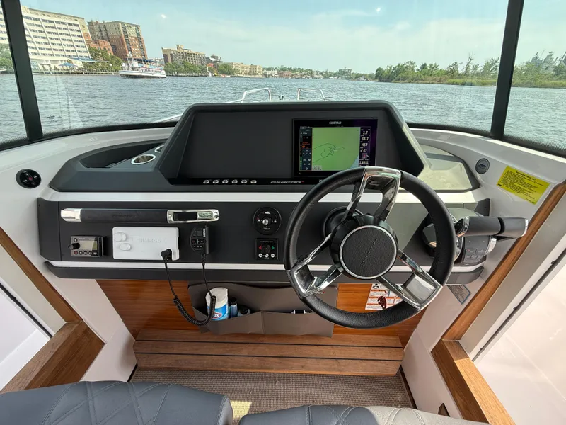 Slide: The Image of 2021 Axopar 28 CABIN helm with steering wheel and navigation display on a calm waterway. - 14