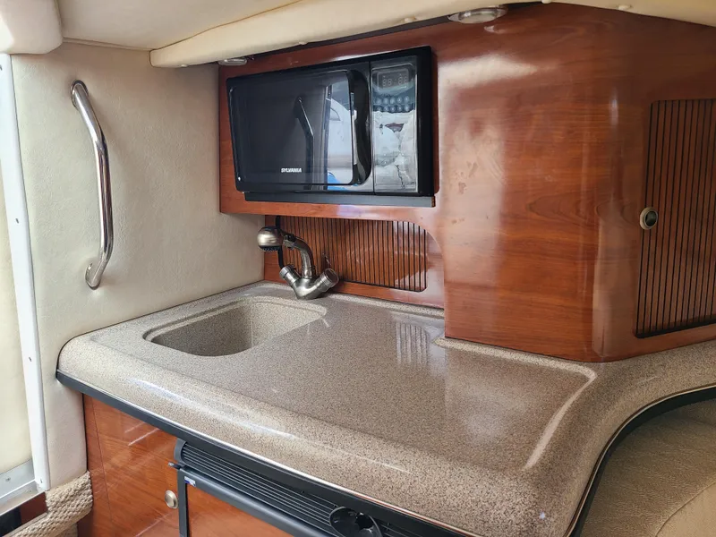 Slide: The Image of 2006 Sea Ray 290 Sun Sport interior with sink and microwave in wooden cabinetry. - 18