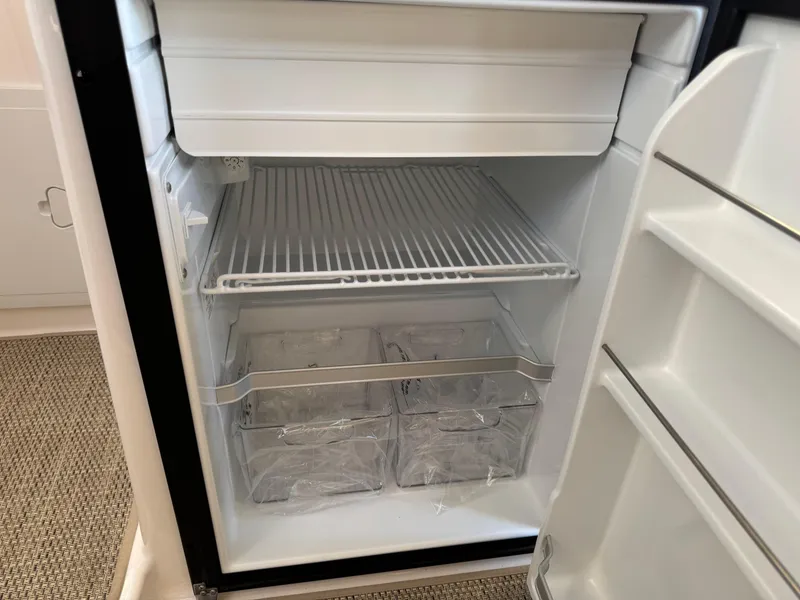 Slide: The Image of Empty refrigerator inside 2025 Cutwater C-288 Coupe boat, featuring wire shelf and storage bins. - 23