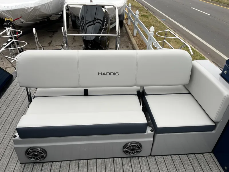 Slide: The Image of 2025 Harris Grand Mariner 250 boat seating with speakers, docked near a road. - 10