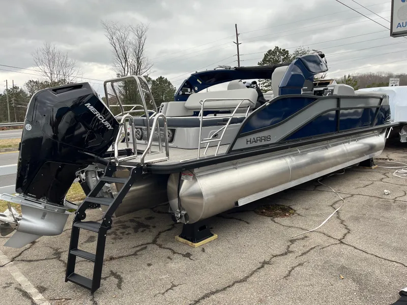 Slide: The Image of 2025 Harris Grand Mariner 250 pontoon boat with Mercury outboard motor, parked on pavement. - 2