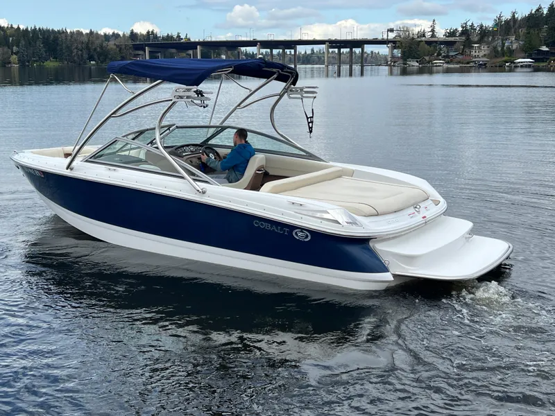 Slide: The Image of 2009 Cobalt 230 boat cruising on a calm lake with a bridge in the background. - 2