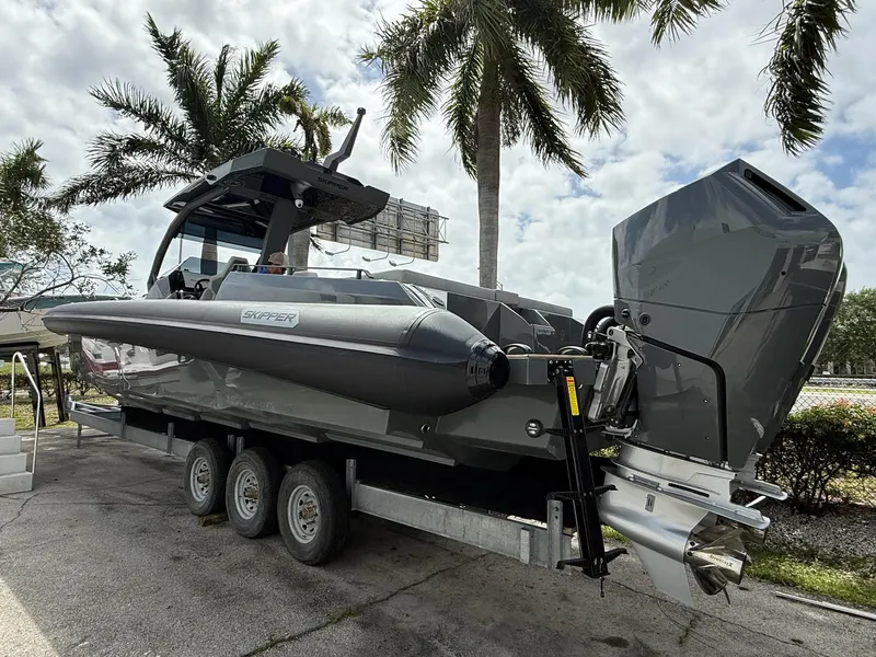 Slide: The Image of 2025 Skipper-BSK 38 boat on trailer, parked under palm trees, showcasing sleek design and powerful engine. - 16