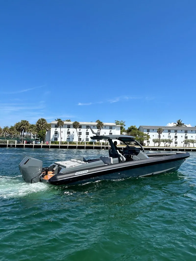 Slide: The Image of 2025 Skipper-BSK 38 boat cruising on clear blue water near waterfront buildings. - 2