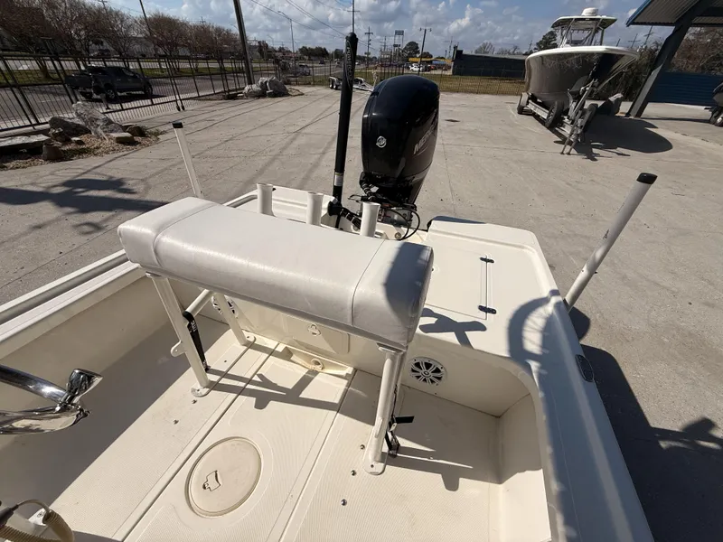 Slide: The Image of 2021 Mako 18 LTS boat interior with seating and motor, parked outdoors. - 17