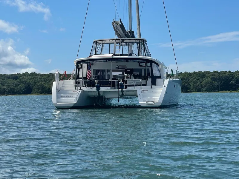 Slide: The Image of 2019 Lagoon 450 F catamaran on calm water, with lush green shoreline in the background. - 2