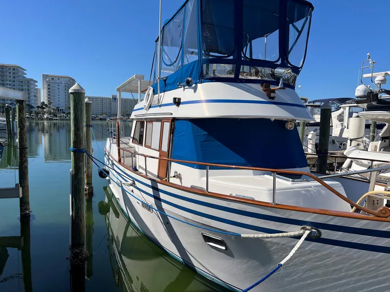 Slide: The Image of 1983 Lindmark 39 Trawler docked in marina, featuring blue canopy and wooden accents. - 2