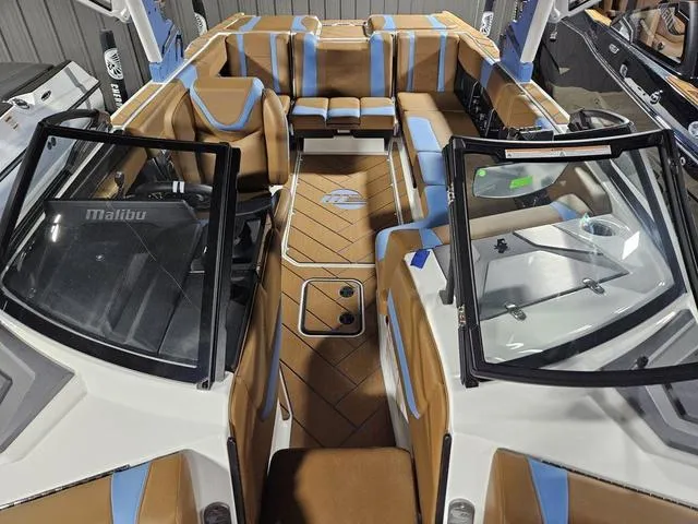 Slide: The Image of 2025 Malibu 23 LSV boat interior with tan and blue seating, open windshield, and sleek design. - 23