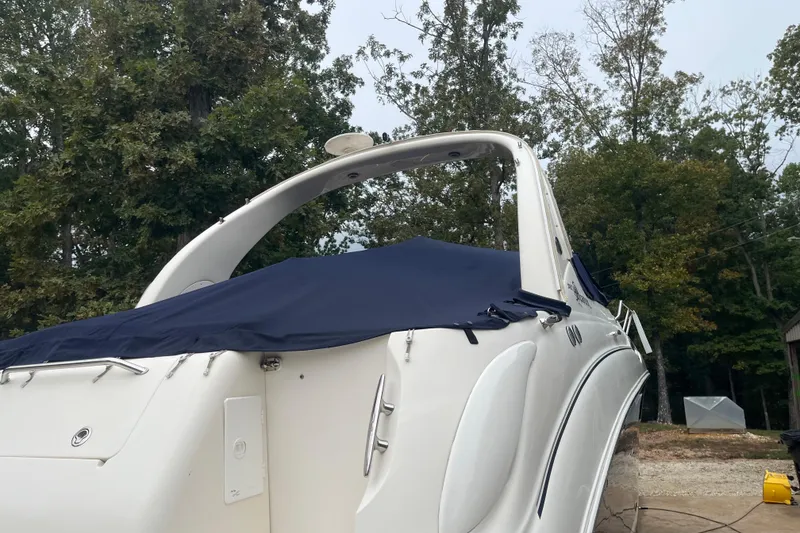 Slide: The Image of 2005 Sea Ray 280 Sundancer boat with blue cover, surrounded by trees. - 12