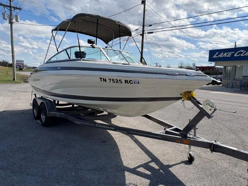 Slide: The Image of 2019 Crownline 215 SS boat on trailer, parked outdoors under a cloudy sky. - 19
