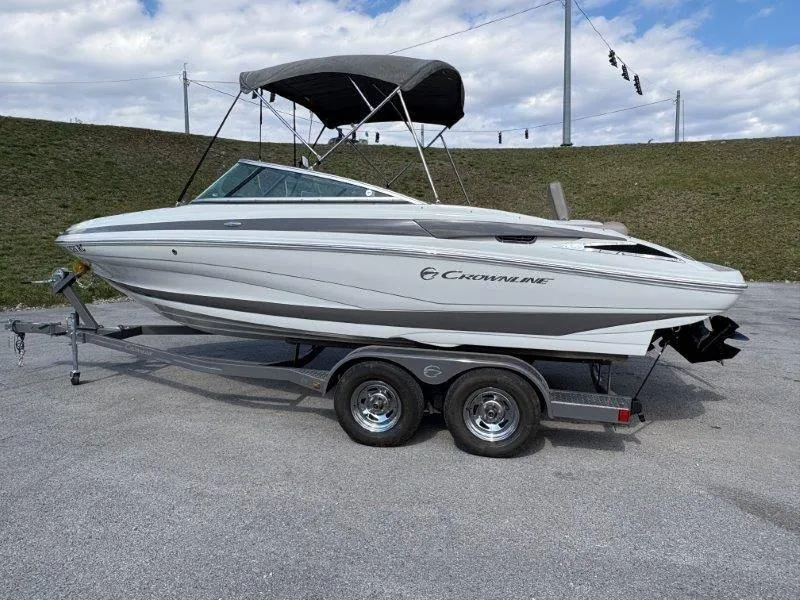 Slide: The Image of 2019 Crownline 215 SS boat on trailer, parked outdoors under cloudy sky. - 27
