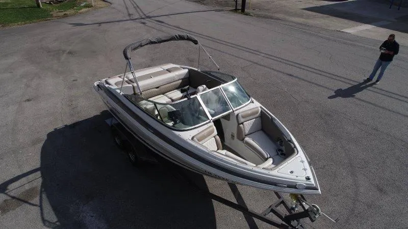 Slide: The Image of 2019 Crownline 215 SS boat on trailer, parked on asphalt, with bimini top. - 7