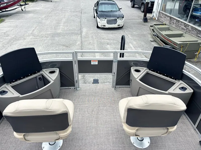 Slide: The Image of 2025 Sun Tracker Fishin' Barge 20 DLX with beige seats and storage compartments, parked near vehicles. - 14