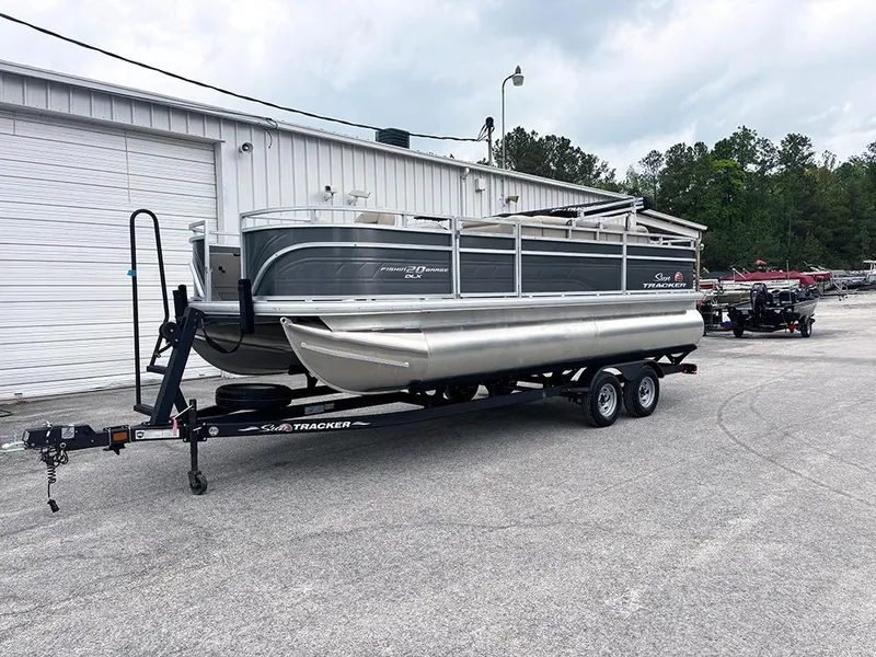 Slide: The Image of 2025 Sun Tracker Fishin' Barge 20 DLX pontoon boat on a trailer near a warehouse. - 3