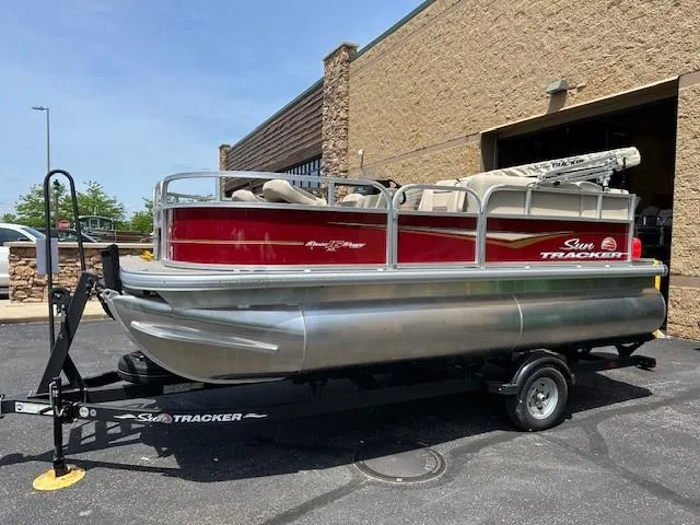 Slide: The Image of 2025 Sun Tracker Bass Buggy 16 XL Select pontoon boat on trailer, parked outdoors. - 2