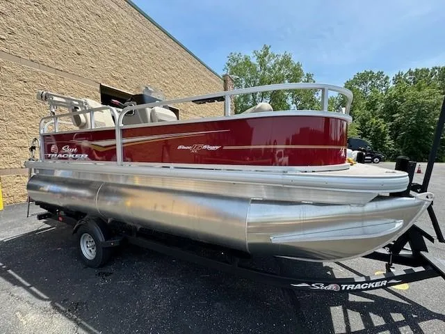 Slide: The Image of 2025 Sun Tracker Bass Buggy 16 XL Select pontoon boat on trailer, parked outdoors. - 3