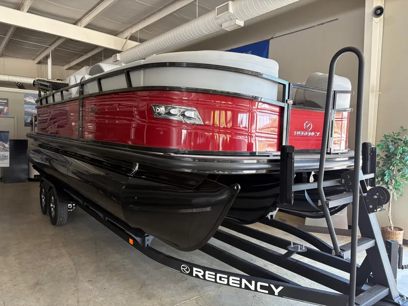 The Image of 2025 Regency 230 DL3 pontoon boat with red exterior on a trailer in a showroom. - 0