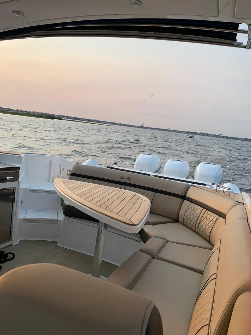 Slide: The Image of 2017 Sea Ray SLX 350 OB boat interior with seating and table, on calm water at sunset. - 14