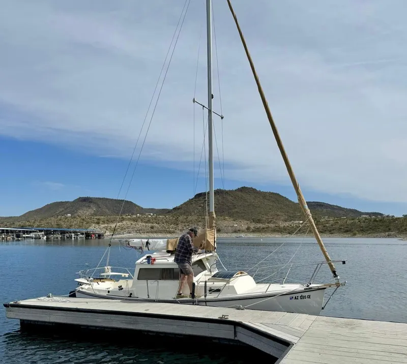 Slide: The Image of 2022 Com-Pac CP 23 Pilothouse sailboat docked on a calm lake with hills in background. - 2