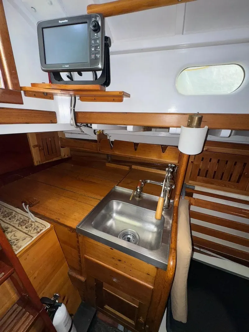 Slide: The Image of Interior of 1955 Concordia 39 Yawl, featuring a compact wooden kitchen with a sink and navigation equipment. - 26