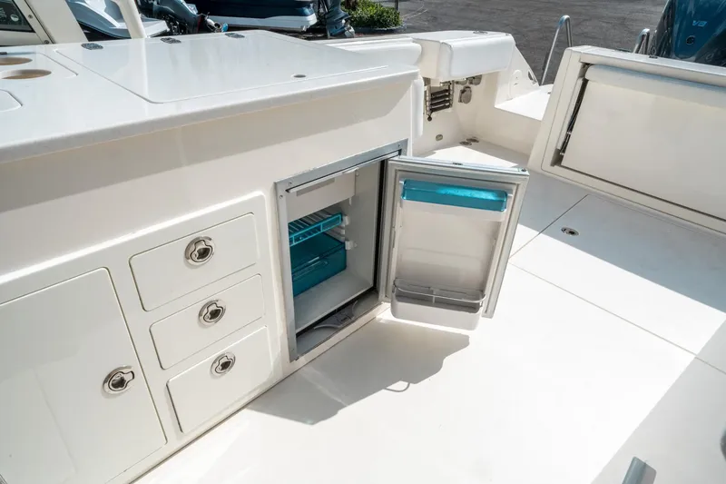 Slide: The Image of 2020 Cobia 330 DC boat interior with open storage compartments and refrigerator. - 23