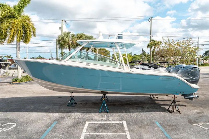 Slide: The Image of 2020 Cobia 330 DC boat on stands, blue hull, palm trees in background. - 5