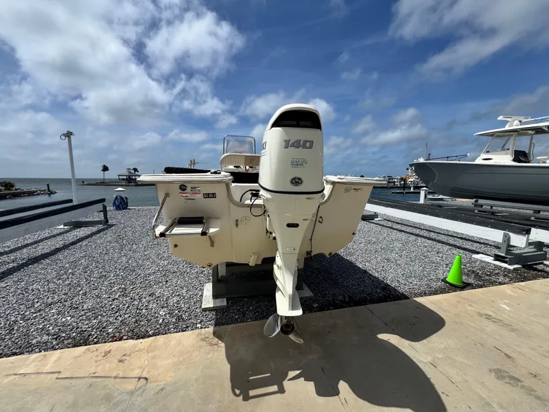 Slide: The Image of 2019 Carolina Skiff 218 DLV boat with outboard motor, parked on gravel near the water. - 4