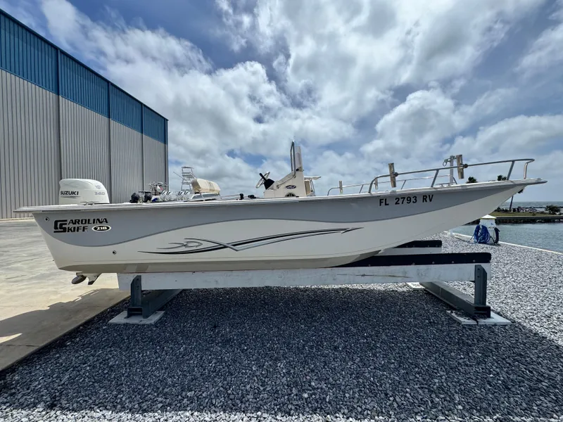 Slide: The Image of 2019 Carolina Skiff 218 DLV boat on display, parked on gravel near a warehouse. - 6