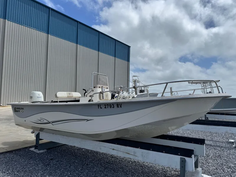Slide: The Image of 2019 Carolina Skiff 218 DLV boat on trailer, parked outdoors under cloudy sky. - 7