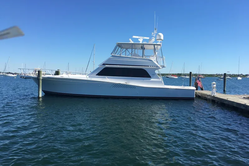 Slide: The Image of 1998 Viking 53 Convertible yacht docked in a serene marina under clear blue skies. - 0