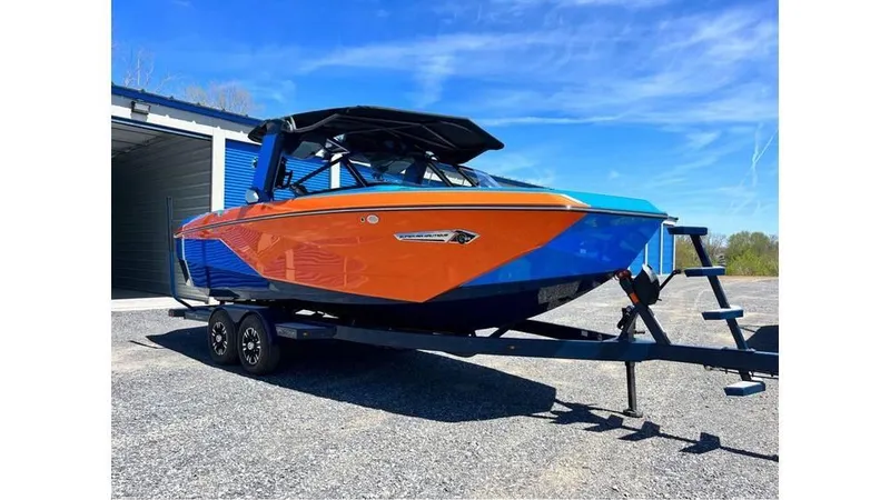 The Image of 2024 Nautique Super Air Nautique G23 boat in vibrant orange and blue, parked on a trailer. - 1