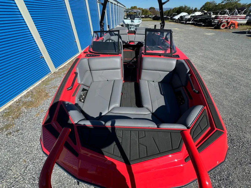 Slide: The Image of 2025 Moomba Tykon boat with red exterior and gray seating, parked near blue storage units. - 3