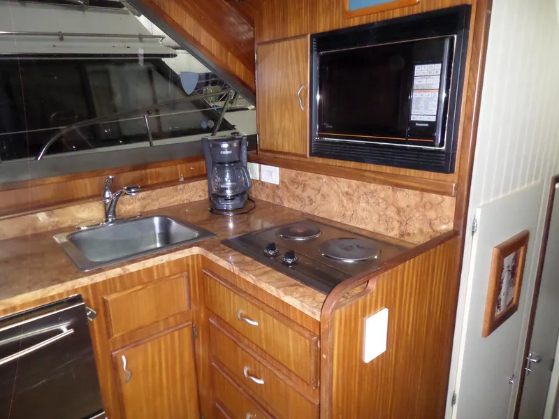 Slide: The Image of 1988 Hatteras 38 Convertible yacht kitchen with sink, stove, microwave, and wooden cabinetry. - 10