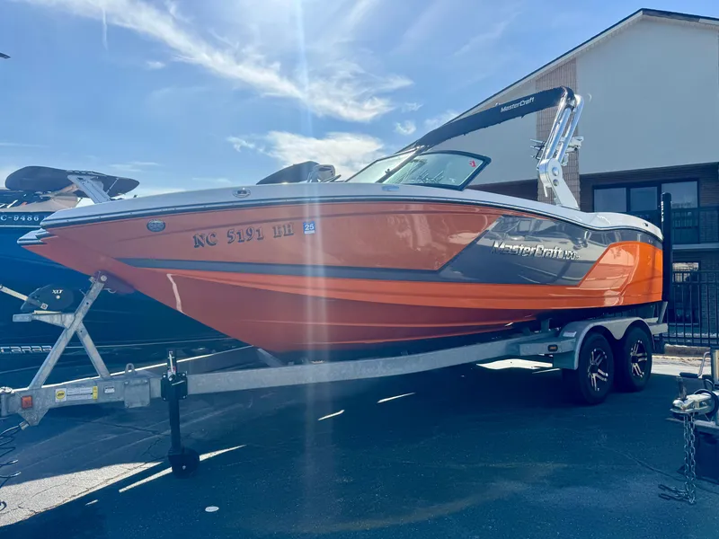 Slide: The Image of 2018 MasterCraft NXT22 boat on trailer, vibrant orange and gray design, parked outdoors. - 0