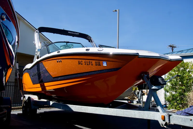 Slide: The Image of 2018 MasterCraft NXT22 boat in vibrant orange on a trailer, under clear blue sky. - 2